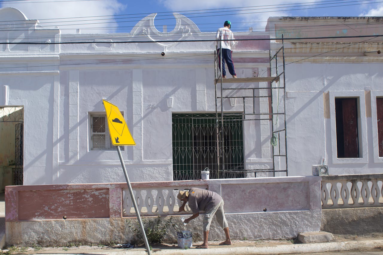 Two men working on a building facade renovation with scaffolding and street sign.