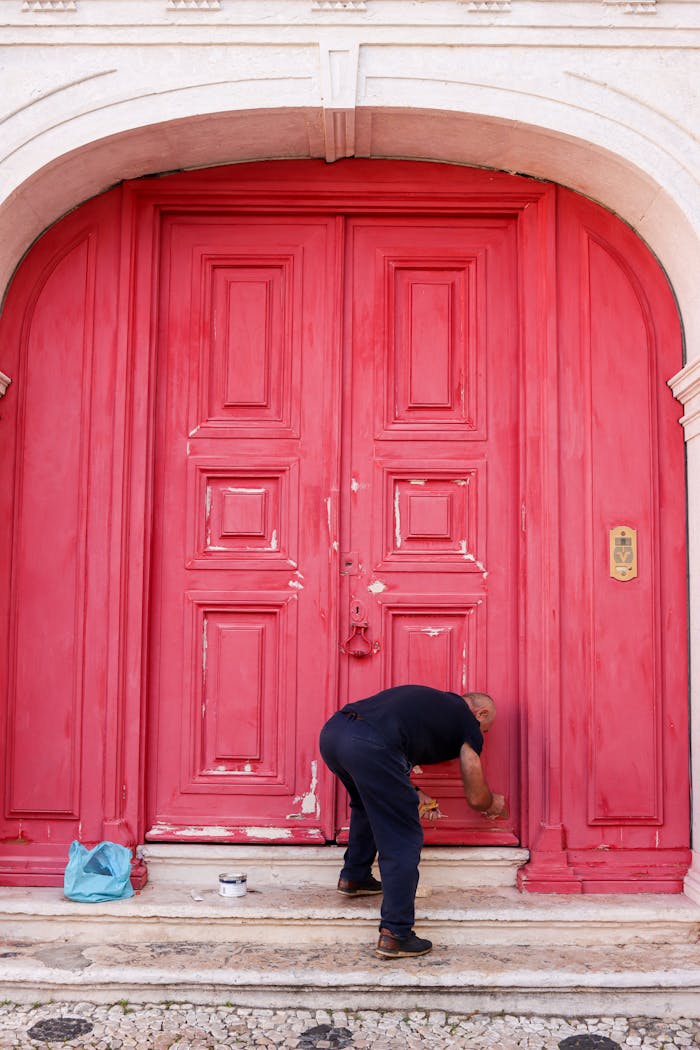 A man paints a vibrant red door on a historic building in Lisbon, Portugal.